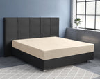 Zandkleurig satijnen hoeslaken op een bed met donker gestoffeerd hoofdbord en boxspring voor een blauwe muur