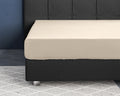 Zandkleurig hoeslaken strak over een matras op een donkergrijs boxspringbed met gecapitonneerd hoofdbord