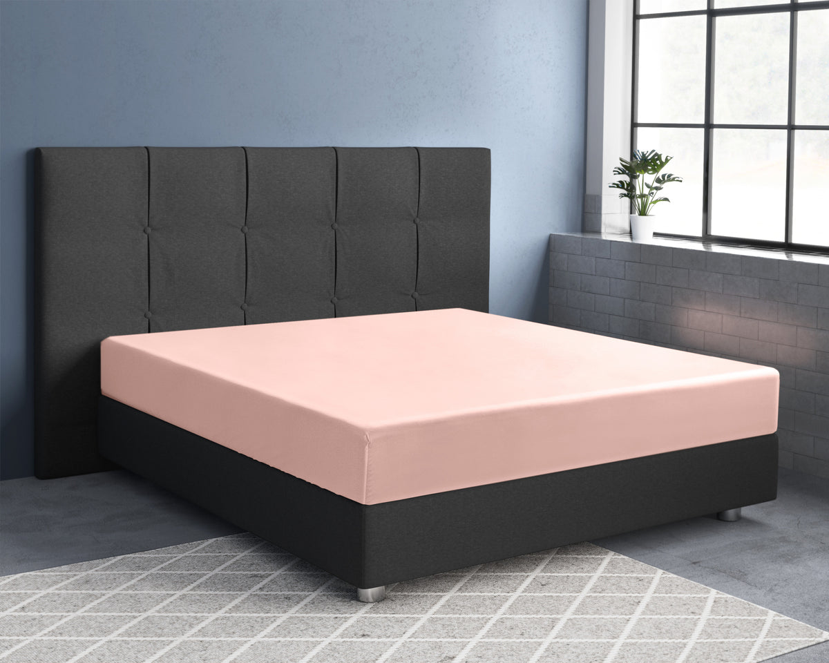 Roze hoeslaken van katoensatijn op een bed met donker gestoffeerd hoofdbord in een slaapkamer met blauwe muur