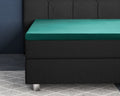 Donkergroen satijnen hoeslaken om een topper op een zwarte boxspring met gestoffeerd hoofdbord