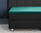 Donkergroen satijnen topper hoeslaken over een topper op een zwart gestoffeerd boxspringbed