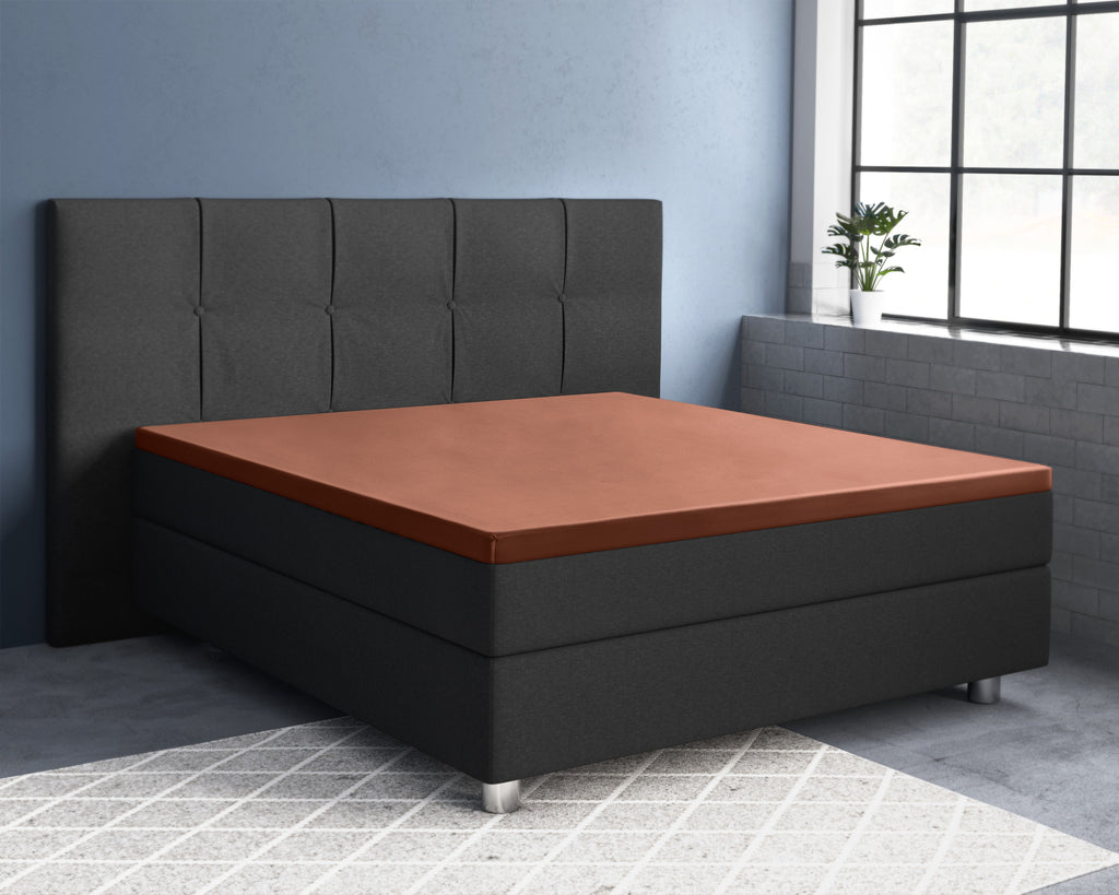 Bruin satijnen hoeslaken op een boxspring met donkergrijs gecapitonneerd hoofdbord in een blauwgrijze slaapkamer