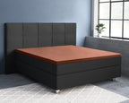 Bruin satijnen topper-hoeslaken op een antracietkleurig boxspringbed met gestoffeerd hoofdbord voor een blauwe muur