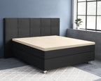 Zandkleurig hoeslaken over de topper van een zwarte boxspring met gestoffeerd hoofdbord in een blauwe slaapkamer