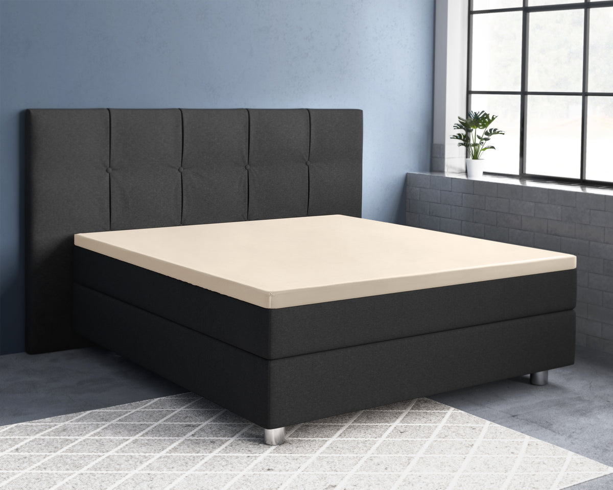 Zandkleurig hoeslaken over de topper van een zwarte boxspring met gestoffeerd hoofdbord in een blauwe slaapkamer