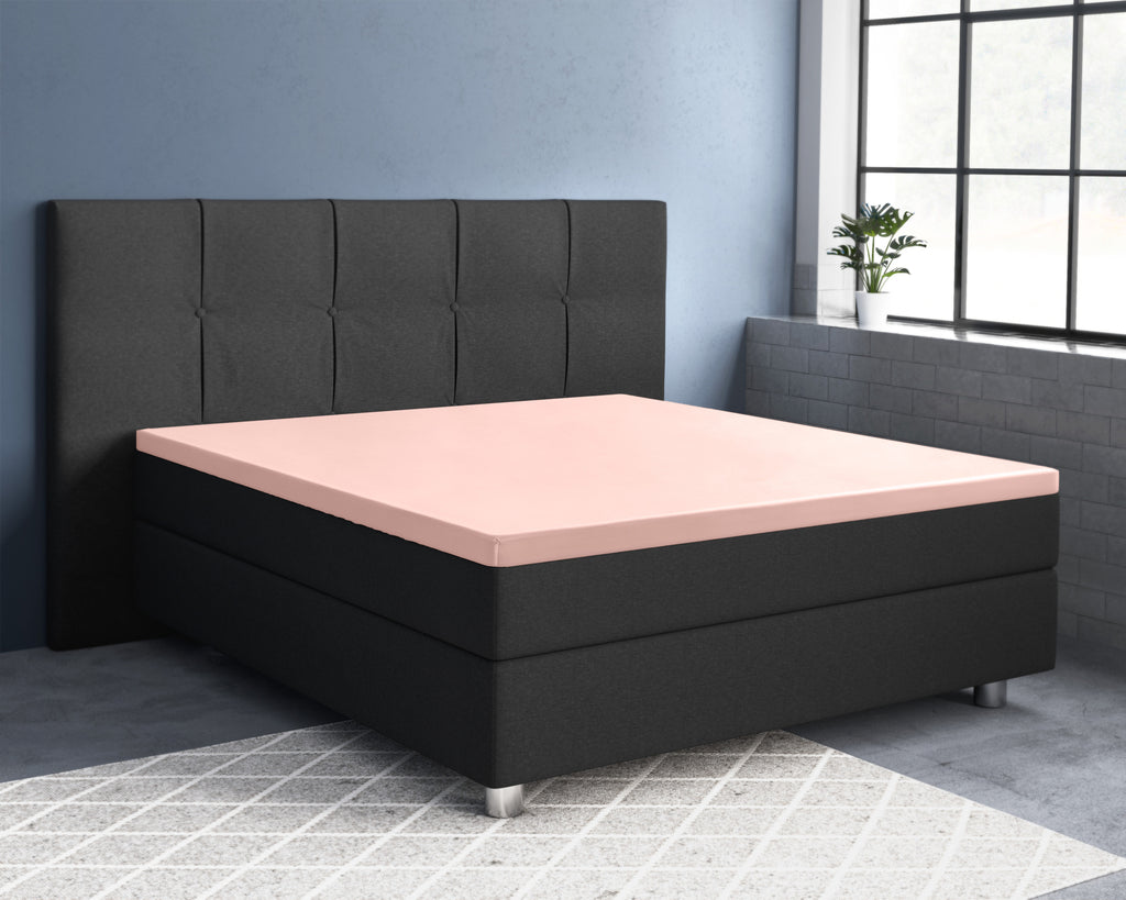 Roze topperhoeslaken op een zwart boxspringbed met gestoffeerd hoofdbord in een slaapkamer met blauwgrijze muur