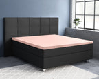 Roze topperhoeslaken op een zwart boxspringbed met gestoffeerd hoofdbord in een slaapkamer met blauwgrijze muur
