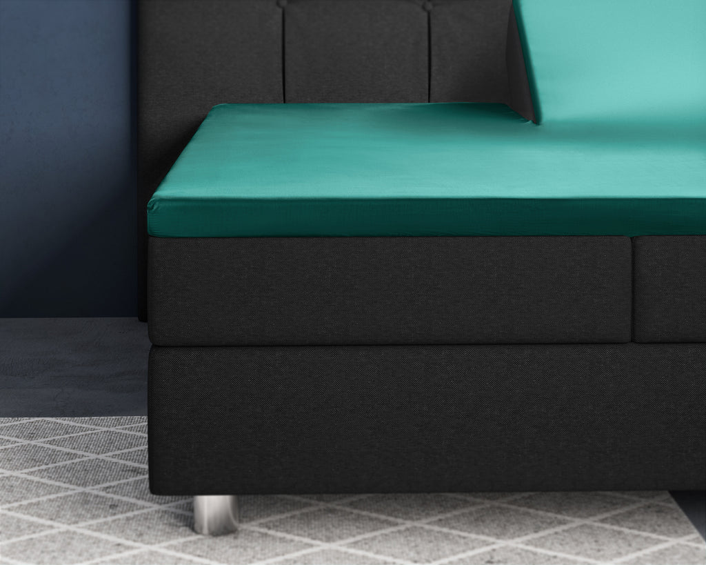 Donkergroen satijnen splittopper hoeslaken op een zwarte boxspring met een opgeklapt hoofdeind