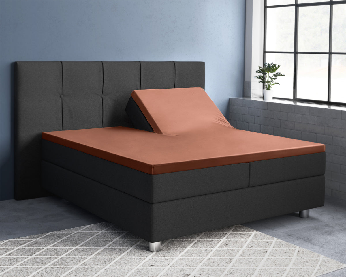 Bruin satijnen splittopper hoeslaken op een donkergrijs bed, met het hoofdeinde van één helft omhoog gesteld