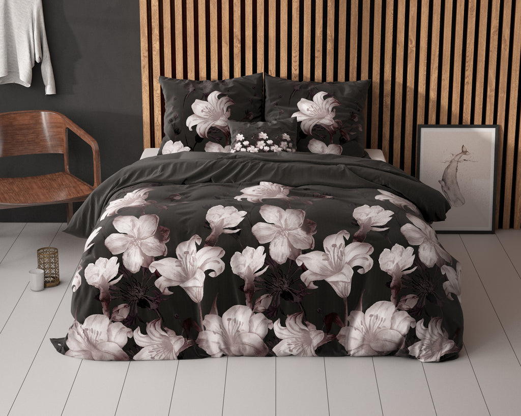 Zwart dekbedovertrek met grote lichte lelies op een bed met houten lamellenwand erachter