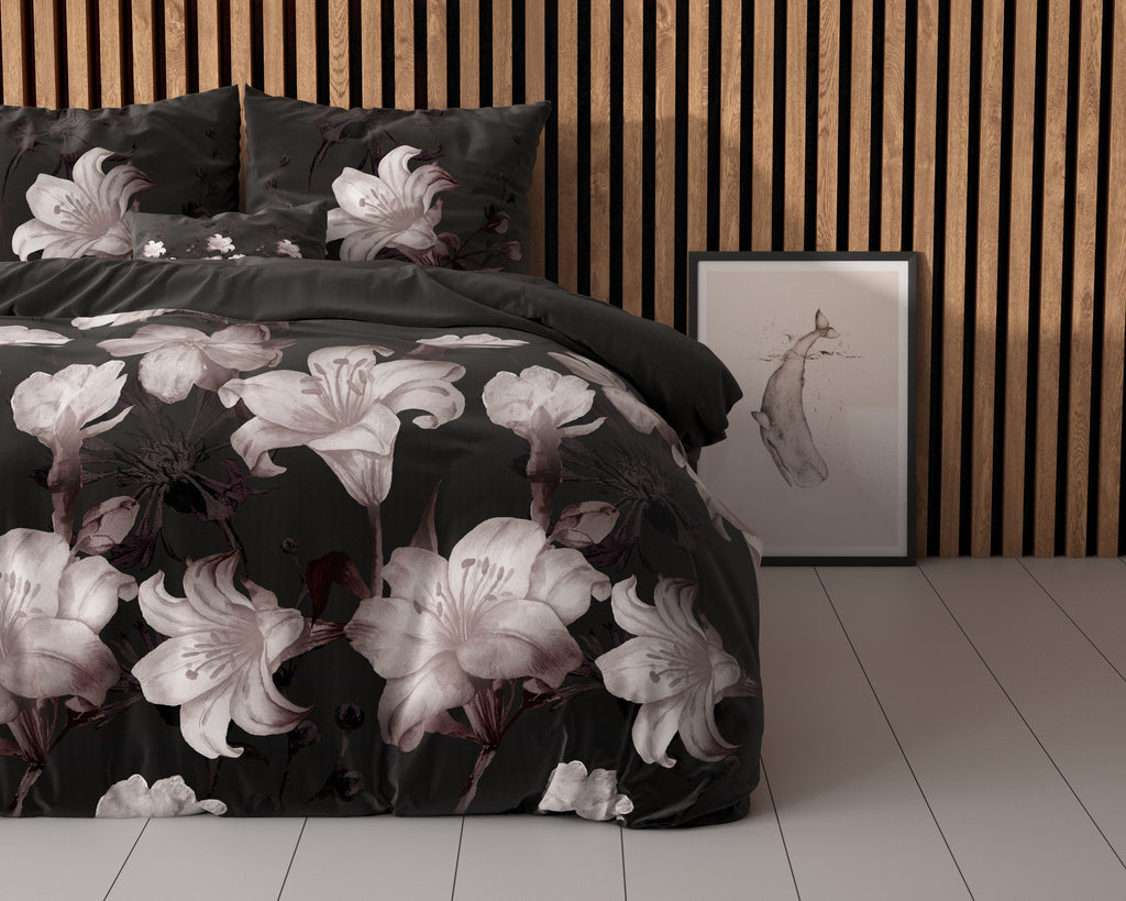 Zwart dekbedovertrek met grote roze-witte lelies op een bed voor een houten lamellenwand