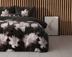 Zwart dekbedovertrek met grote roze-witte lelies op een bed voor een houten lamellenwand