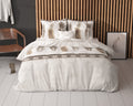 Bed met wit-beige dekbedovertrek met verenprint en kussens voor een houten lamellenwand