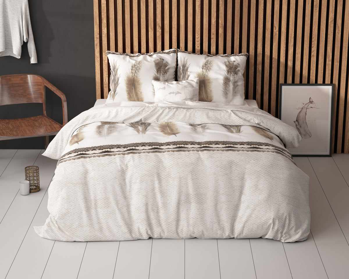 Bed met wit-beige dekbedovertrek met verenprint en kussens voor een houten lamellenwand