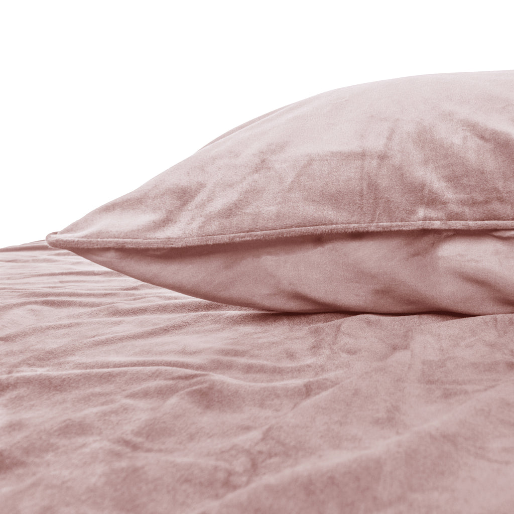 Roze fluwelen kussen met paspelrand op een bed met bijpassend roze fluwelen dekbedovertrek