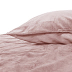 Roze fluwelen kussen met paspelrand op een bed met bijpassend roze fluwelen dekbedovertrek