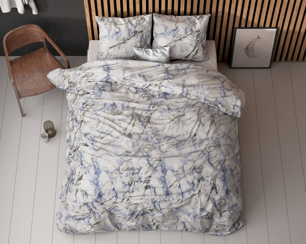 Dekbedovertrek met blauw-grijs marmerprint op een bed met kussens, gezien van boven, naast een houten stoel
