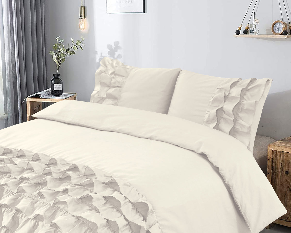 Crèmekleurig dekbedovertrek met ruches en bijpassende kussenslopen op een bed in een lichte slaapkamer