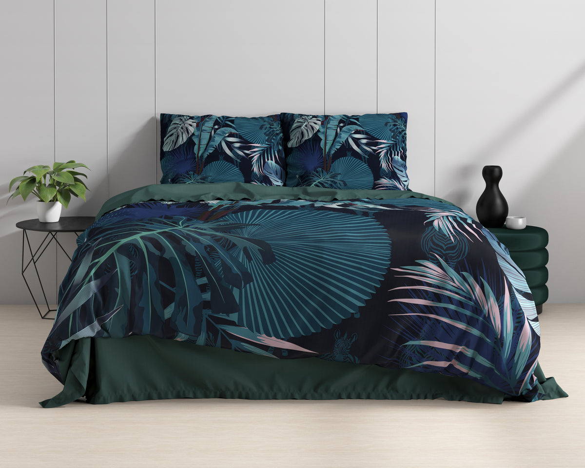 Opgemaakt bed met dekbedovertrek met botanische bladprint in blauw en teal, naast plant en zwarte bijzettafel