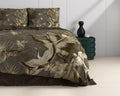 Bed met taupe dekbedovertrek met print van kraanvogels en palmbladeren, naast een groen nachtkastje met zwarte vaas