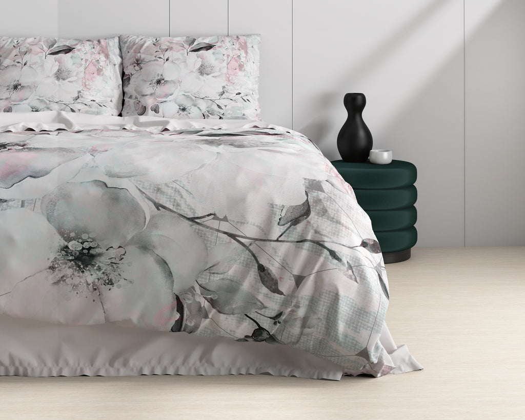 Opgemaakt bed met wit dekbedovertrek met grijs-roze bloemenprint, naast een groene poef met zwarte vaas
