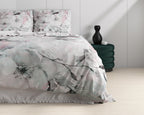 Opgemaakt bed met wit dekbedovertrek met grijs-roze bloemenprint, naast een groene poef met zwarte vaas
