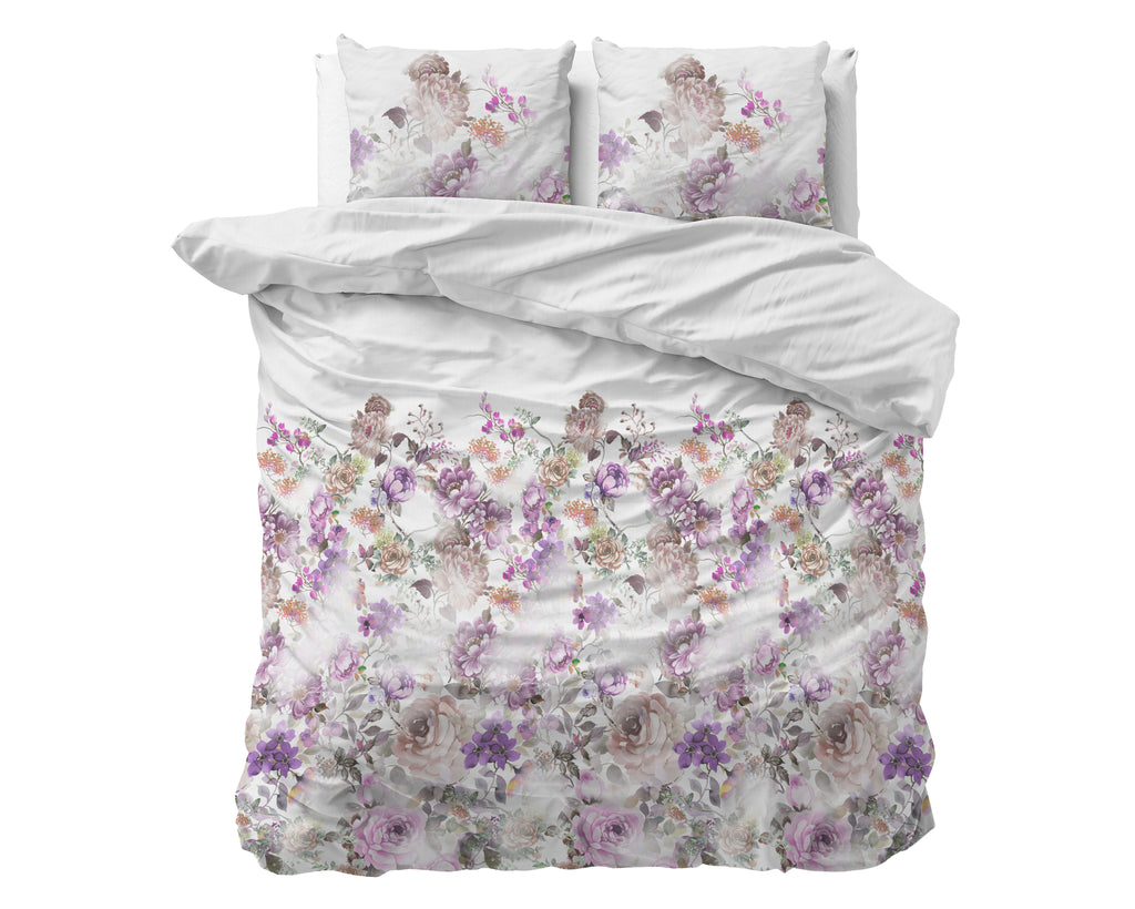 Bed opgemaakt met wit dekbedovertrek met roze en paarse bloemenprint en twee bijpassende kussens