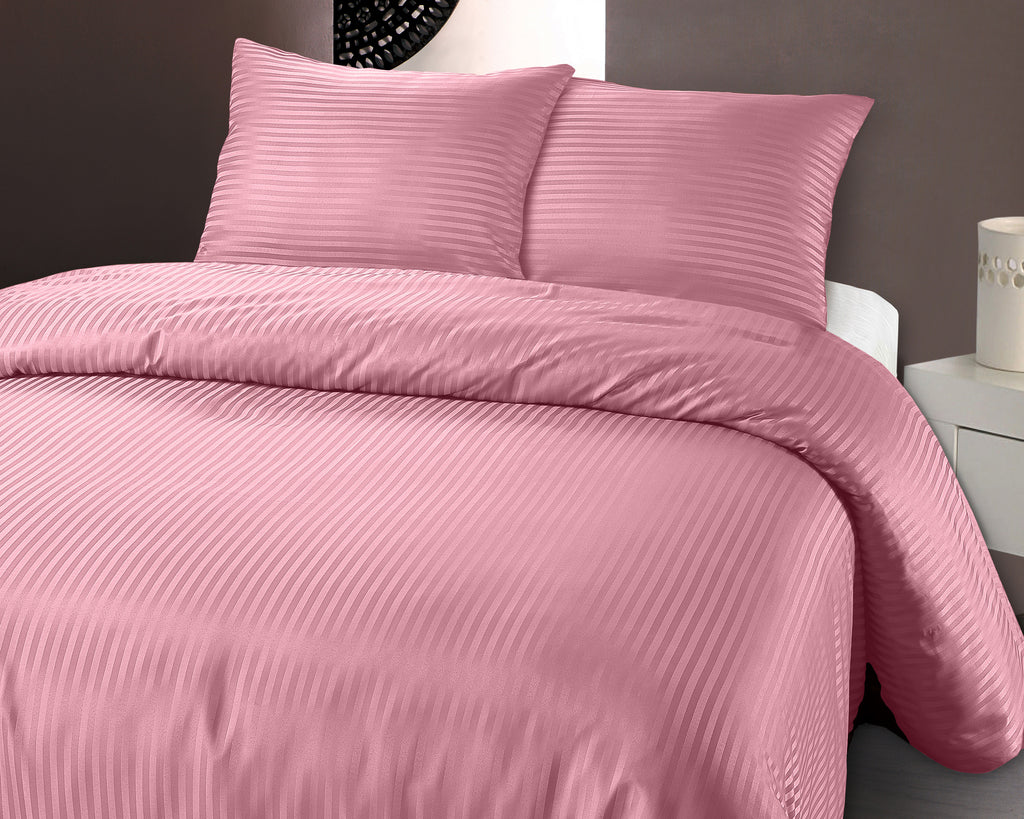 Roze geëmbosseerd dekbedovertrek met fijne strepen en twee bijpassende kussens op een bed
