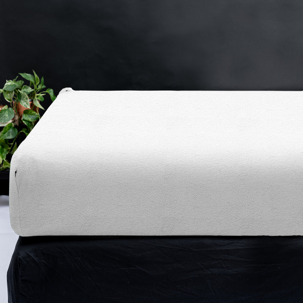 Wit teddy hoeslaken over een matras, naast een plant tegen een donkere achtergrond