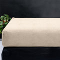 Taupe teddy hoeslaken om een matras, met een groene plant op de achtergrond