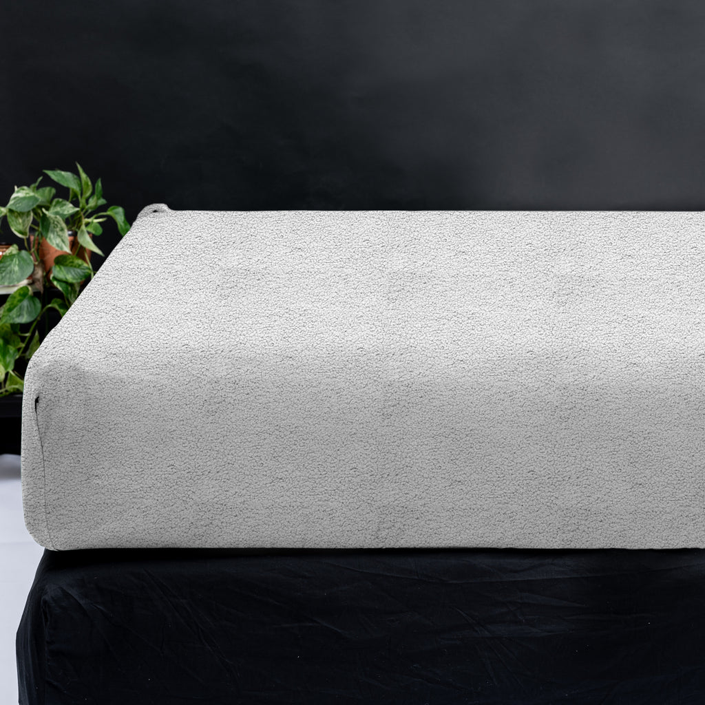 Grijs teddy hoeslaken over een matras op een zwart bed, naast een groene kamerplant