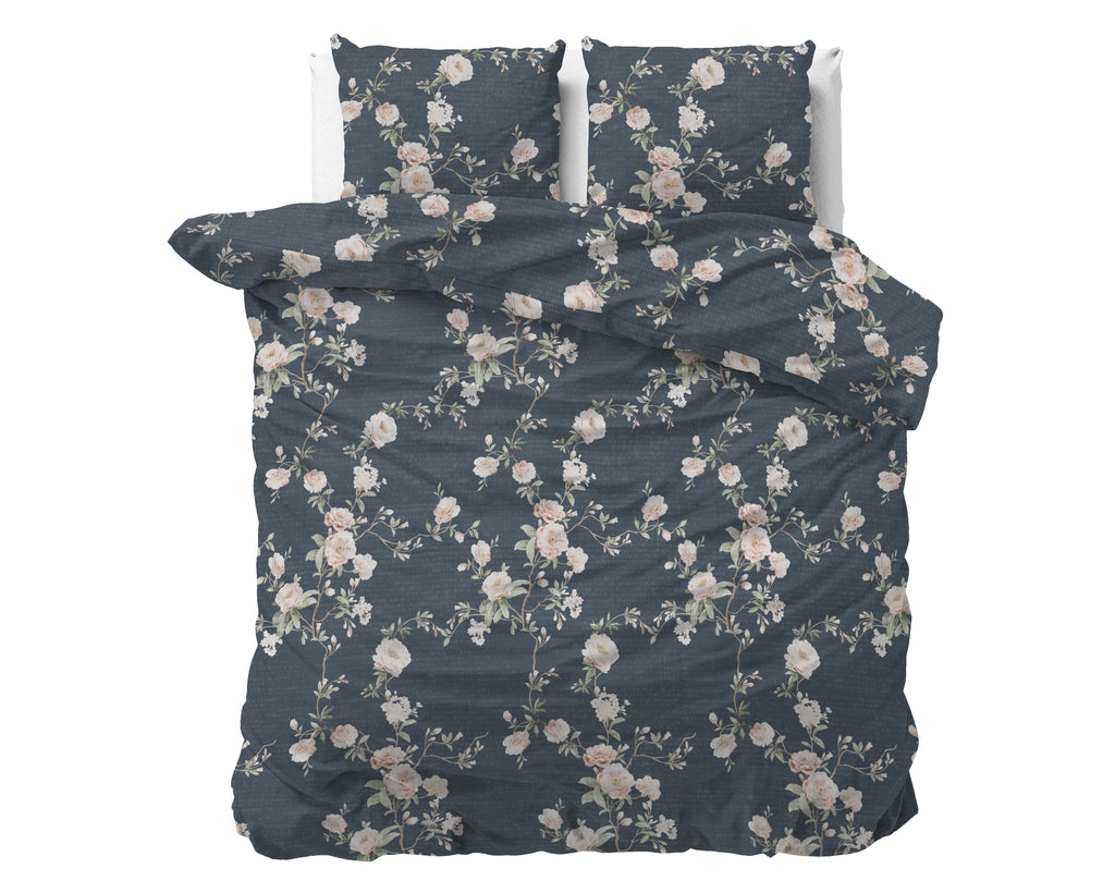 Opgemaakt bed met indigo dekbedovertrek en twee kussens met roze en witte bloemenprint