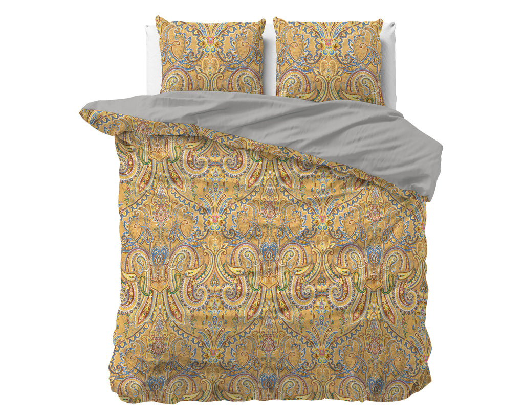 Dekbedovertrek met goudgele paisleyprint en grijze achterzijde, met twee bijpassende kussens op een bed