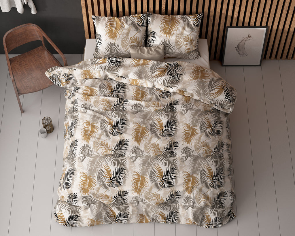 Bed met dekbedovertrek met palmbladprint in zand, goud, grijs en zwart, met twee kussens tegen een houten lamellenwand