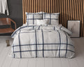 Bed met wit dekbedovertrek met donkerblauw en lichtblauw ruitdessin voor een houten lamellenwand