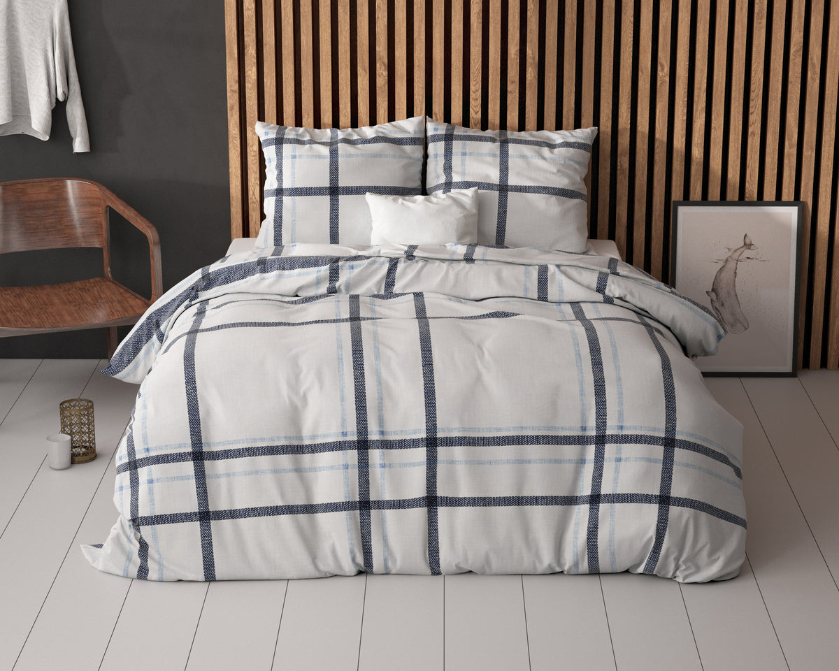 Bed met wit dekbedovertrek met donkerblauw en lichtblauw ruitdessin voor een houten lamellenwand
