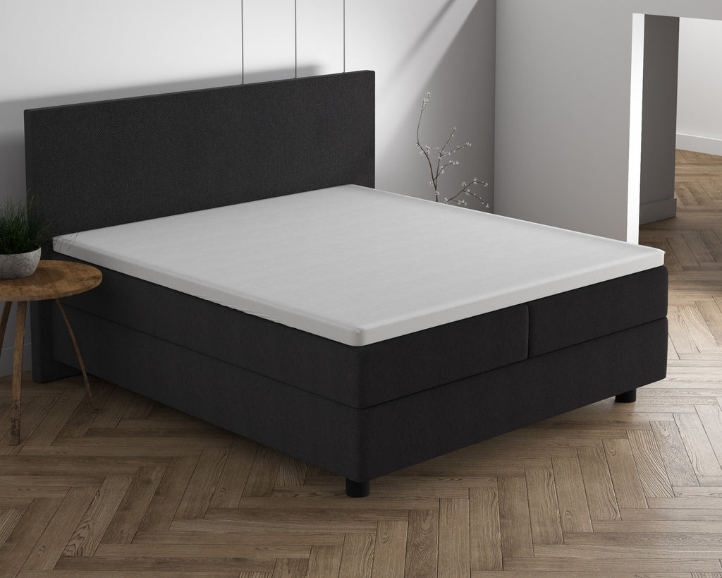 Wit topper op een antracietkleurig boxspringbed met bijpassend hoofdbord in een lichte slaapkamer met visgraatvloer