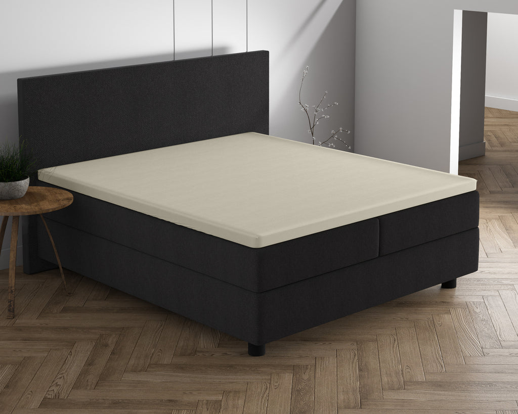 Crèmekleurig topper hoeslaken op een donkergrijs boxspringbed met hoofdbord in een lichte slaapkamer