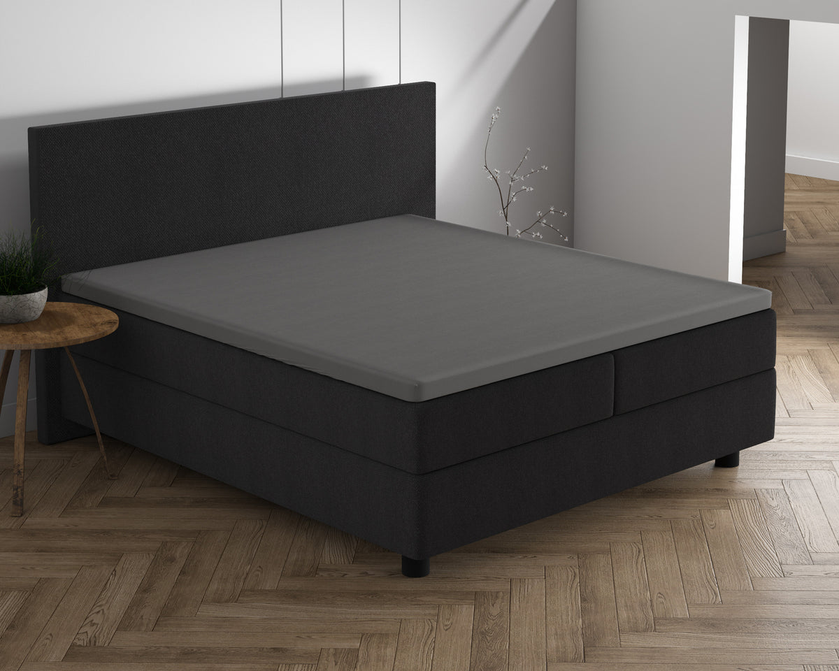 Grijs topper hoeslaken op een boxspring met donker hoofdbord in een slaapkamer met visgraatvloer