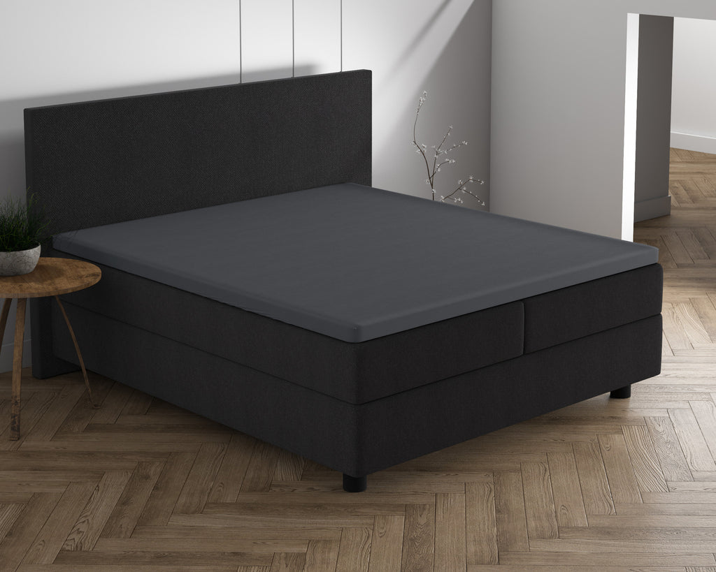 Antraciet topper hoeslaken op een donkere boxspring met bijpassend hoofdbord in een slaapkamer met visgraatvloer
