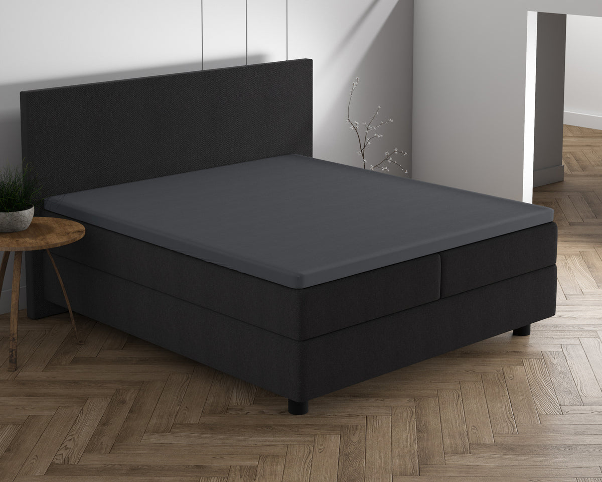 Antraciet topper hoeslaken op een donkere boxspring met bijpassend hoofdbord in een slaapkamer met visgraatvloer