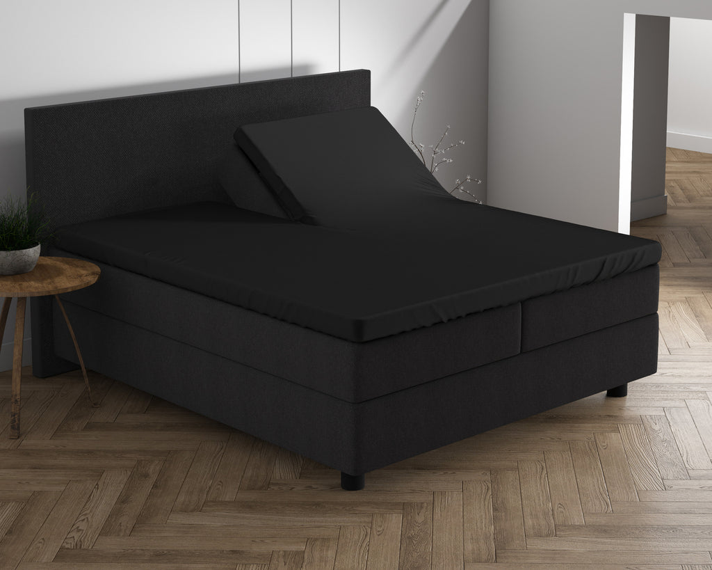 Zwart hoeslaken op een split-topper van een donker boxspringbed, met één helft van de topper omhoog gezet