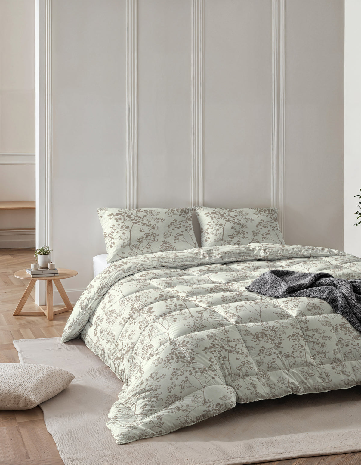Opgemaakt bed met groen alles-in-één dekbed met takjesprint en twee bijpassende kussens, met een grijs plaid erover