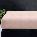 Roze teddy hoeslaken over een matras tegen een donkere achtergrond, met een groene plant links