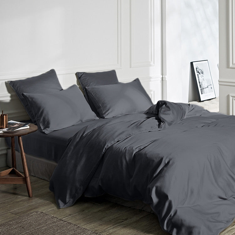 Opgemaakt bed met antracietkleurig dekbedovertrek, bijpassende kussenslopen en hoeslaken naast een houten bijzettafel