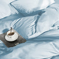 Blauw dekbedovertrek met kussens op een bed, met een kopje koffie op een tijdschrift