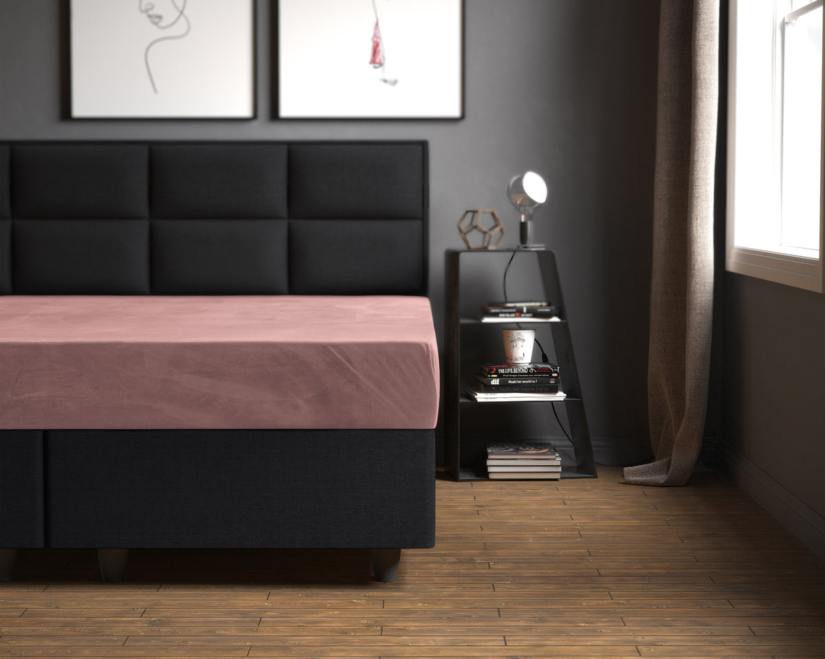 Oudroze velours hoeslaken op een bed met donker gestoffeerd hoofdbord en boxspring in een grijze slaapkamer