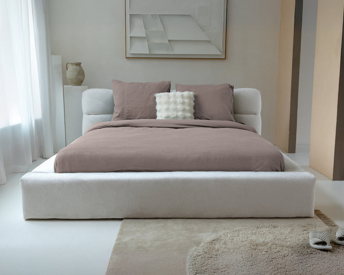 Taupe dekbedovertrek met wafelstructuur en bijpassende kussenslopen op een bed met lichte bouclé bedombouw
