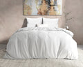 Wit flanel dekbedovertrek op een opgemaakt bed met witte kussens, voor een beige muur met een schilderij