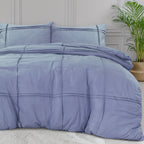 Blauw dekbedovertrek met plooidetails en twee kussens op een bed, naast een plant in rieten mand
